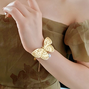 Detail of vintage gold butterfly bracelet with white pearl charm on model's wrist