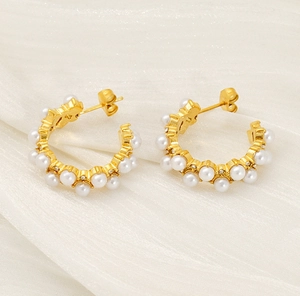Detail of C-shaped gold pearl earrings with zircon stones on silk fabric background