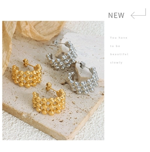 Detail of layered gold and silver C-shaped bead earrings on a textured stone display