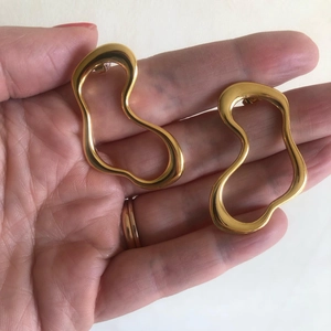 Close-up of chunky gold irregular hollow hoop earrings held in hand with sleek metallic texture