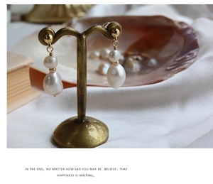 Baroque pearl earrings hanging on a vintage brass stand with silk and shell background