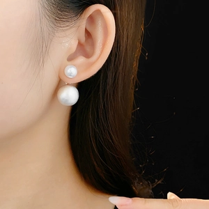 Close-up of elegant double-sided white pearl earrings on model with black background