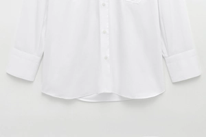 Detail of curved hem and buttoned cuff on a classic white long sleeve cotton shirt