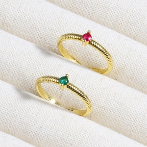 Close-up of gold rings with red and green round gemstones on a textured jewelry tray