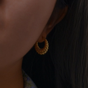 Close-up of a gold croissant hoop earring with a vintage screw design on a female model