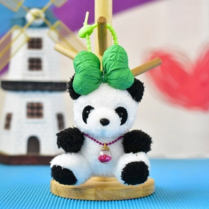 Detail of a panda plush keychain featuring a green head bow and red bead necklace.