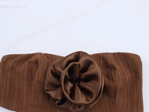 Detail of coffee brown ruched fabric featuring a large satin 3D flower decoration