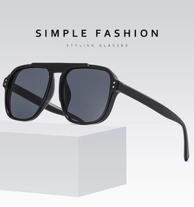 Minimalist black aviator sunglasses with grey lenses on a white geometric block pedestal