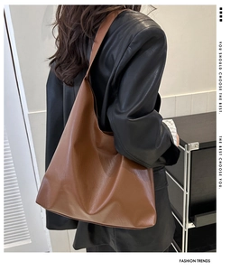 Gros plan détaillé d'un grand sac hobo en cuir marron porté avec un manteau en cuir
