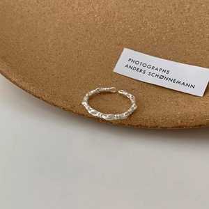 Detailed close-up of a silver braided texture open ring on a wooden display plate