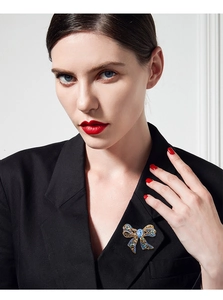 Detailed close-up of luxury gold bow brooch with blue gemstones on black suit lapel