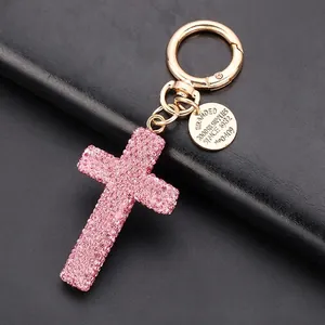 Pink rhinestone cross keychain with gold alloy base and leather cord on black background