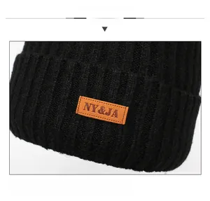 Detailed close-up of black ribbed knit beanie featuring an orange leather brand tag