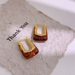 Detail shot of U-shaped gold-plated hoop earrings with amber resin and metal texture