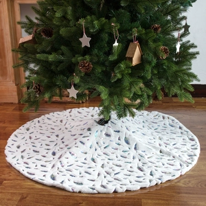 White plush Christmas tree skirt with gold feather print in a cozy holiday home setting