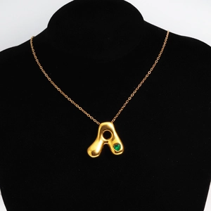 Close-up of golden bubble letter A pendant with a green heart-shaped gemstone
