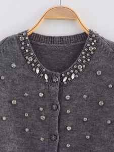 Close-up of rhinestones and knitting texture on a dark grey round neck cardigan