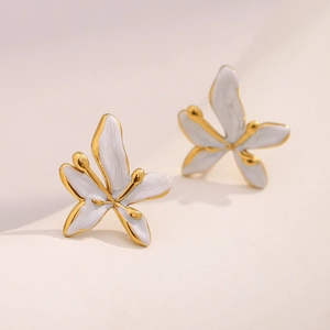 Macro shot of gold-plated flower stud earrings with elegant white enamel finish