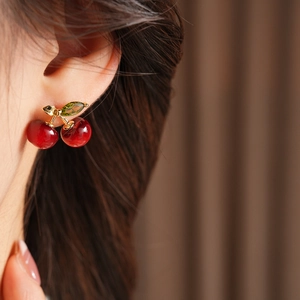 Detail of cherry stud earring with red resin fruits and sparkling green zircon leaf