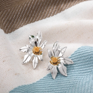 Detailed macro shot of flower stud earrings with silver petals and golden center on striped fabric