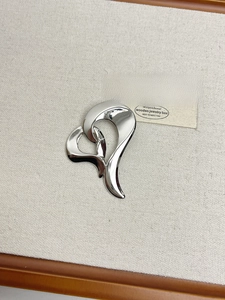 Macro detail of polished silver abstract heart brooch on a linen textured display stand