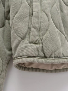 Détail macro du matelassage en losanges et texture sergé d'une veste vert sauge