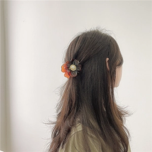 Detail of floral hair claw clip with amber petals and pearl center on long hair