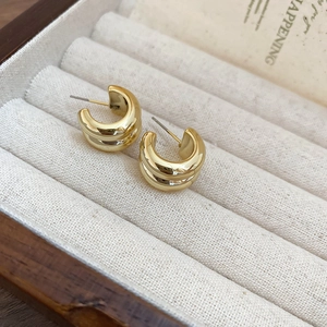 Detail of minimalist double-layered golden C-shaped earrings on cream velvet display