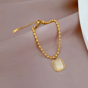 Detail eines Goldperlenarmbands mit quadratischem Katzenaugenstein auf lila Stoff