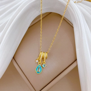Gold titanium necklace with blue water-drop pendant and crystals in a beige jewelry box
