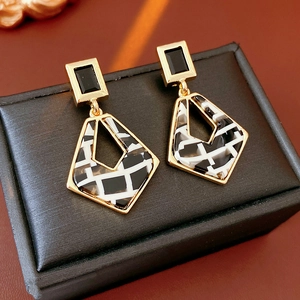 Close-up of geometric resin earrings with black squares and checkered rhombuses on leather