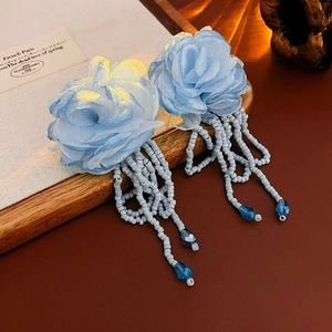 Detail of light blue fabric flower earrings with beaded tassels and a teardrop pendant