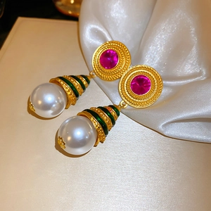 Macro shot of vintage gold earrings with pink gemstones, green enamel, and large white pearls