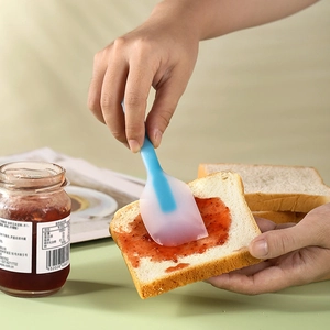 Blue translucent silicone spatula spreading strawberry jam on white toast bread