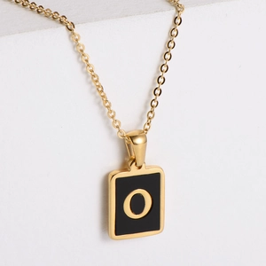 Macro shot of a gold square pendant necklace featuring a black face and golden letter O
