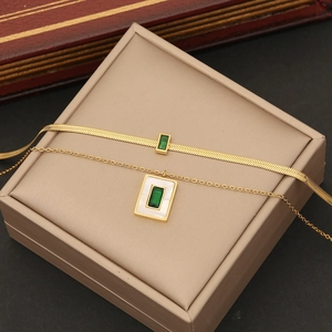 Detail of double-layered gold necklace with emerald green rectangular gemstone pendants