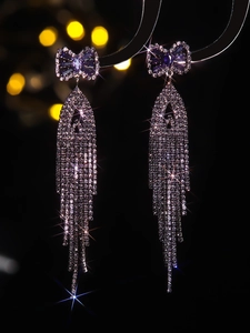 Macro shot of silver bow earrings featuring purple zircon and cascading tassel rhinestones