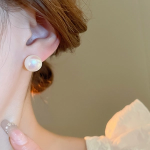 Close-up of model wearing elegant round iridescent pearl stud earrings with golden plating