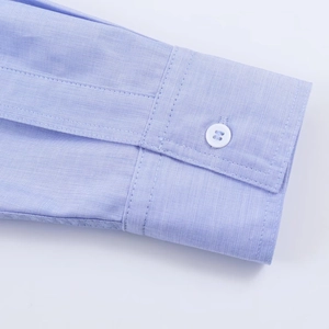 Dettaglio del polsino della camicia celeste con bottone bianco e trama fine del tessuto