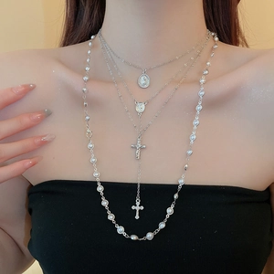 Close-up of layered silver cross and pearl necklace set worn on a model's neck
