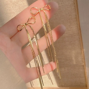 Close-up of hand holding golden bow-knot earrings with long hanging metal tassels