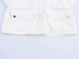 Detail of white utility jacket featuring two flap pockets and circular metal snap buttons
