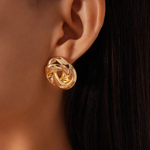 Close-up of golden intertwined knot stud earrings worn by a model for a chic metallic look
