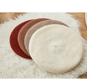 Woolen beret hats in white, beige, coffee, and brick red on a soft plush and wood floor