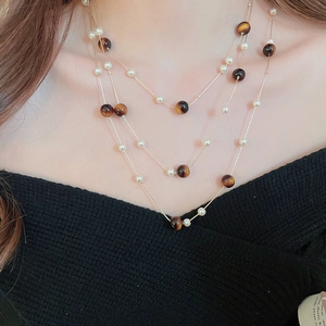 Détail d'un collier doré multicouche avec perles blanches et perles œil de tigre vintage