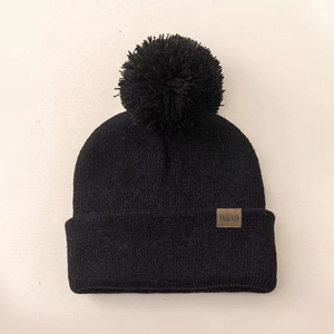 Solid black knit beanie with a faux fur pompom and Fashion leather label for kids