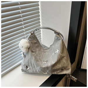 Detail of silver pleated shoulder bag with metal butterfly charms and plush pendant