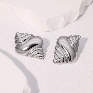 Detailed macro view of silver conch shell earrings on a white textured stone surface