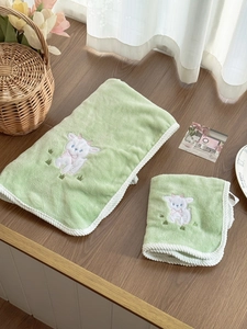 Detail of light green lamb-embroidered bath towels with soft plush texture and ribbon