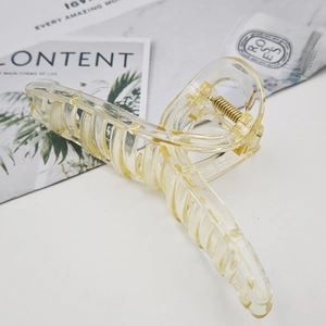 Detail of a large translucent yellow hair claw clip with golden spring on a white desk